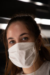 Close-up portrait of a young woman wearing face mask in front of white lights