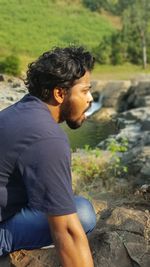 Side view of young man crouching on rock