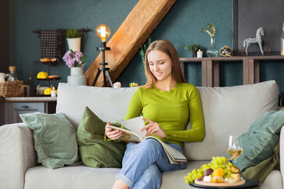 Young woman reading book while sitting on sofa