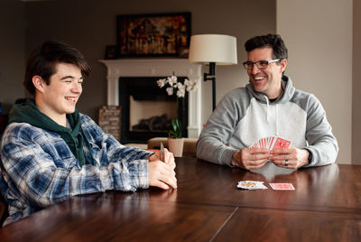 Father and teenage son laughing as they play cards at the table.