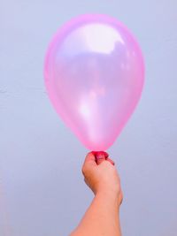 Cropped image of hand holding pink balloons against sky