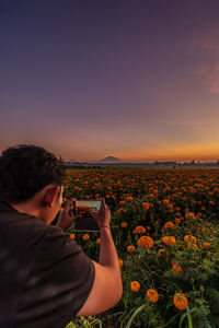 Man photographing field against sky during sunset