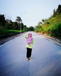 Full length of girl in hijab showing peace sign on road