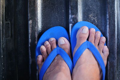 Low section of person wearing blue flip-flop standing on metallic surface