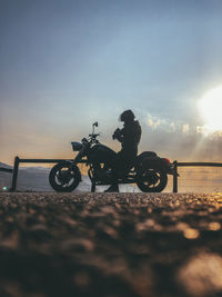 Man riding bicycle on street against sky during sunset