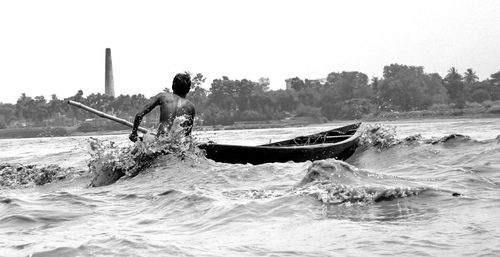 Rear view of man sailing boat in river against sky