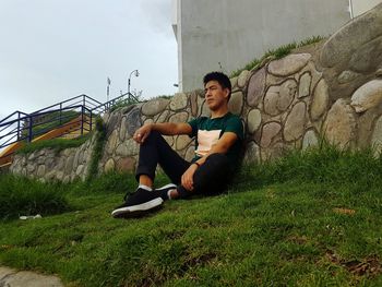 Low angle view of young man sitting on field against wall