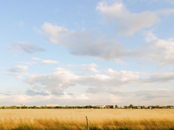 Scenic view of grassy field against cloudy sky on sunny day