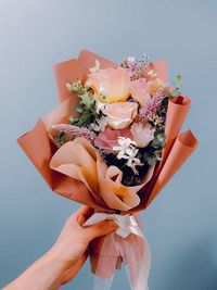 Close-up of hand holding bouquet against blue background
