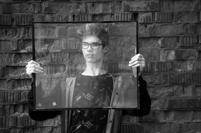 Teenage boy holding glass frame while standing against wall