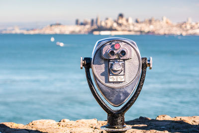 Close-up of coin-operated binoculars by sea against sky