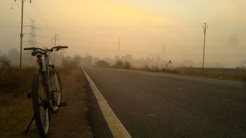 Bicycle parked by road against sky during sunset