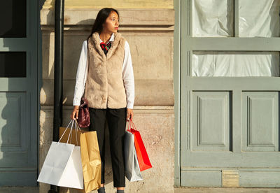 Calm hispanic female shopper with dark hair with shopping bags standing near building with door on sunny street of city