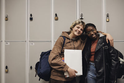 Portrait of smiling female friends standing together against locker in school