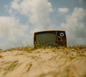 Retro television set on sand against cloudy sky