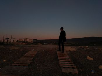 Man standing on shore against sky during sunset