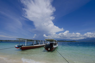 Boat moored in sea against cloudy sky