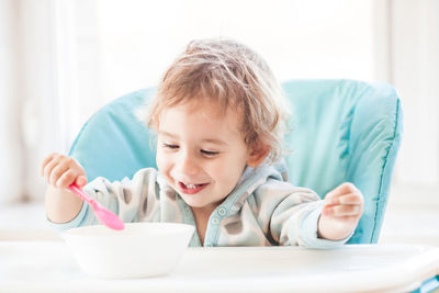 Cute girl with spoon and bowl on table at home