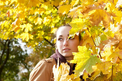 Thoughtful woman standing by trees in park during autumn