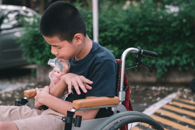 Boy holding doll sitting on wheelchair