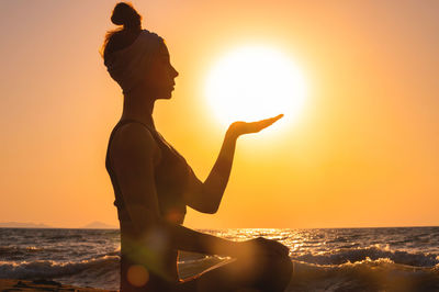Rear view of silhouette woman with arms outstretched against sea during sunset