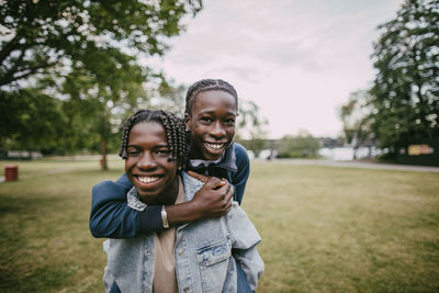 Portrait of braided hair teenage boy piggybacking male friend at park