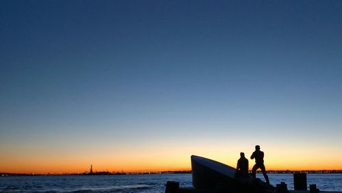 Statues at sea shore against clear sky during sunset