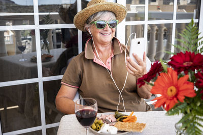 Smiling senior woman listening music while sitting at cafe