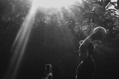 Side view of shirtless man standing against trees in forest