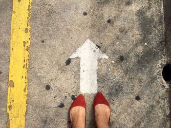 Low section of woman in red flat shoe standing by arrow sign on road