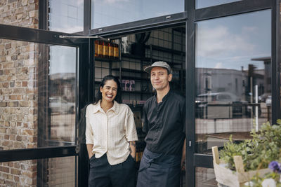 Happy female owner standing with male colleague at cafe doorway