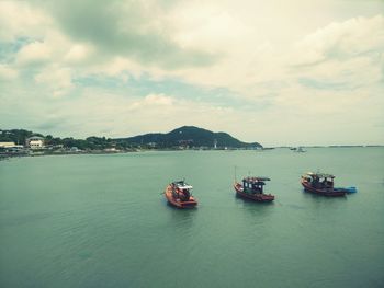 Boats in sea against cloudy sky