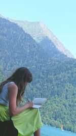 Woman sitting on mountain against clear sky