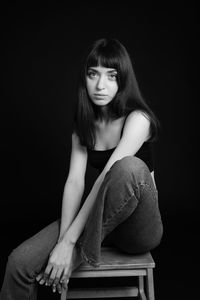 Portrait of woman sitting against black background