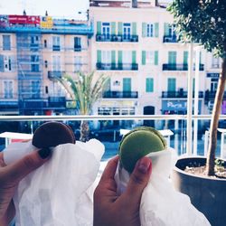 Cropped image of friends holding macaroons against building in city