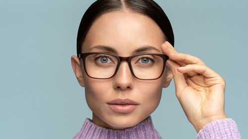 Confident business woman adjusts glasses, looking at camera, isolated on studio blue background. 