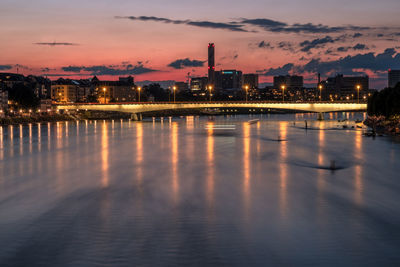 Illuminated city by river against sky during sunset