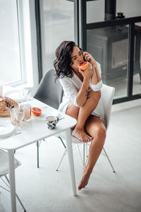 Woman eating fruit while talking over smart phone while sitting on chair at home