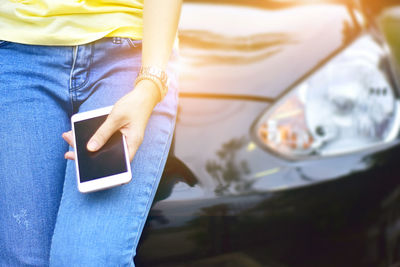 Midsection of woman holding mobile phone while sitting on car