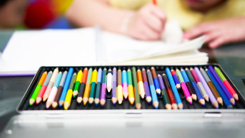 Color pencil crayons of various colors in a palette box, on the table, against the backdrop