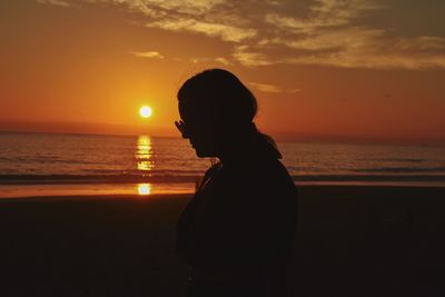 Silhouette woman on beach against sky during sunset