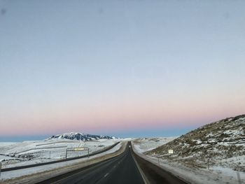 Road amidst snowcapped mountains against clear sky during winter