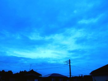 Low angle view of silhouette electricity pylon against blue sky