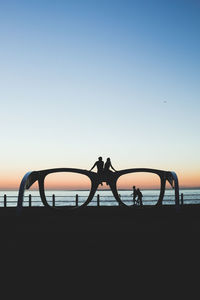 Silhouette men by sea against clear sky during sunset