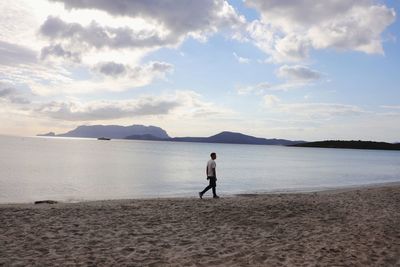 Rear view of man walking at beach against sky during sunset