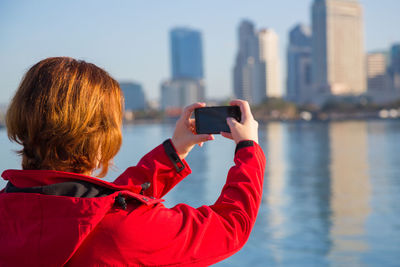 Rear view of woman photographing through smart phone while standing in city