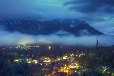 Illuminated houses by mountain against sky