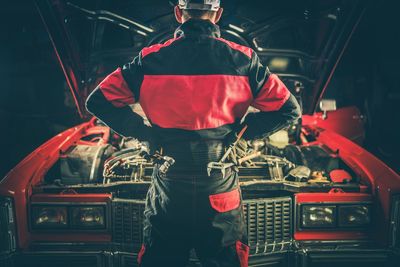 Rear view of mechanic standing by car in workshop