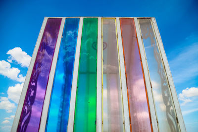 Low angle view of multi colored glass wall against blue sky