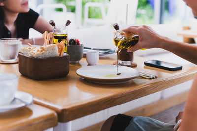 Female hand pouring balsamic vinegar sauce on white plate at dinner table.